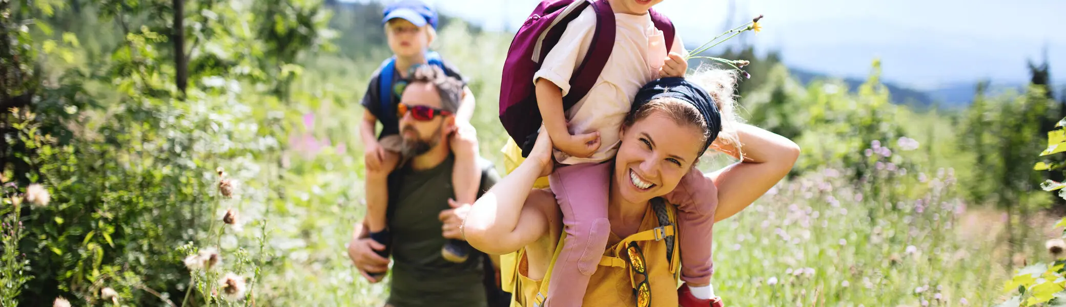 Eine Familie in der Natur, die Mutter trägt ein Kind auf den Schultern | © Halfpoint / Adobe Stock
